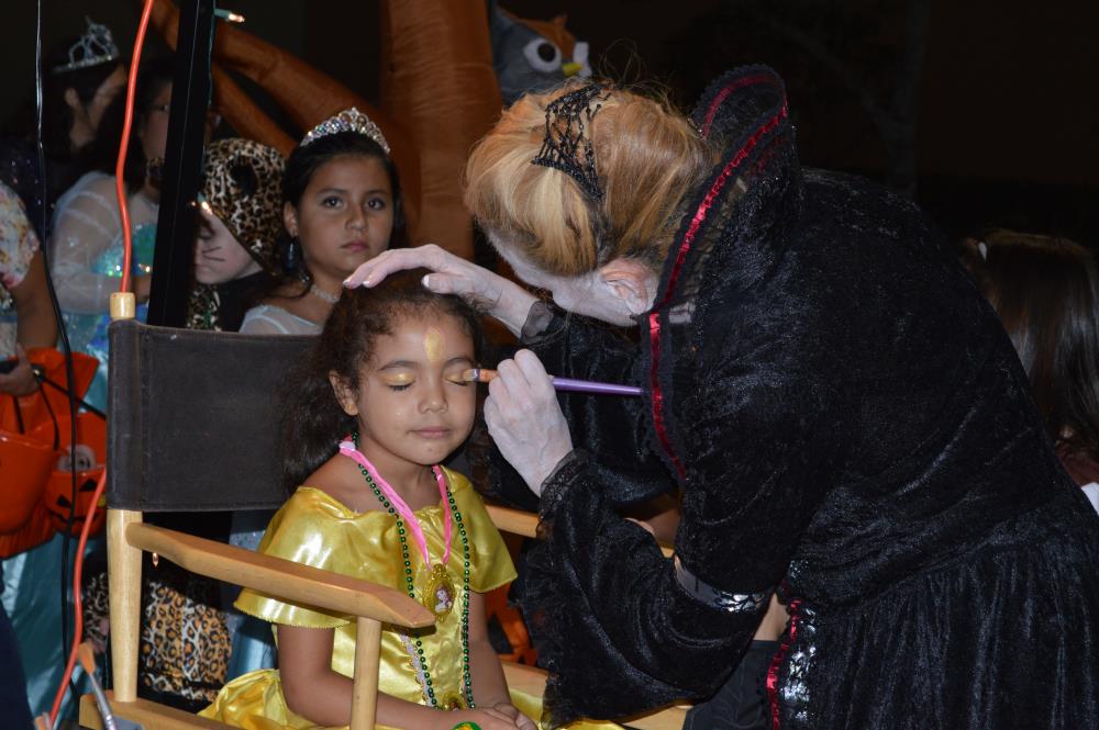 Girl in yellow dress from Beauty and the Beast gets face painted by woman in black dress